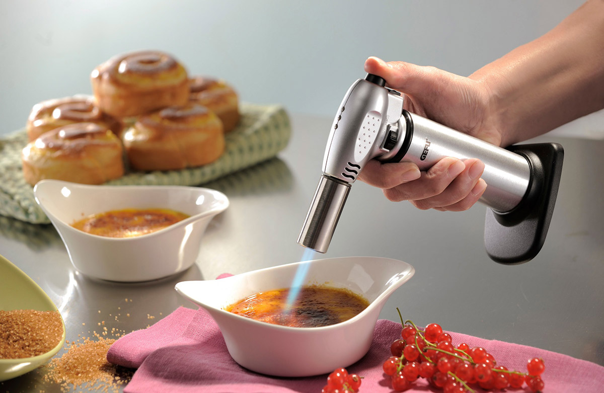 Eine Hand hält eine Küchenfackel, um Zucker auf Crème brûlée zu karamellisieren.