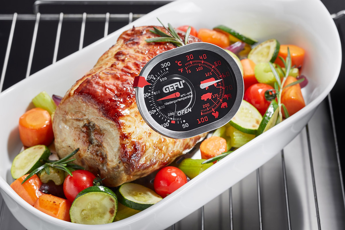 Gebratenes Fleisch in einer weißen Schale mit Gemüse, ein Ofenthermometer steckt im Fleisch.