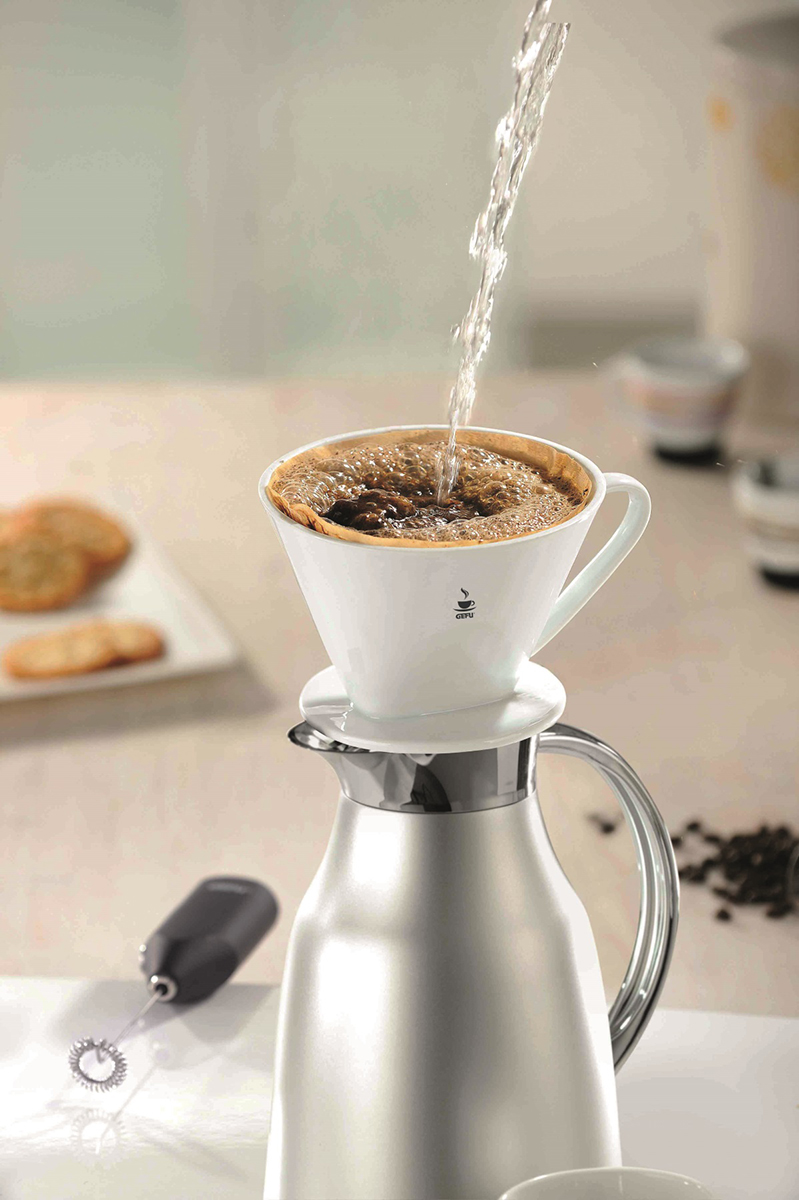 Kaffee wird in einen weißen Dripper über eine silberne Karaffe gegossen. Kaffeezubereitung.