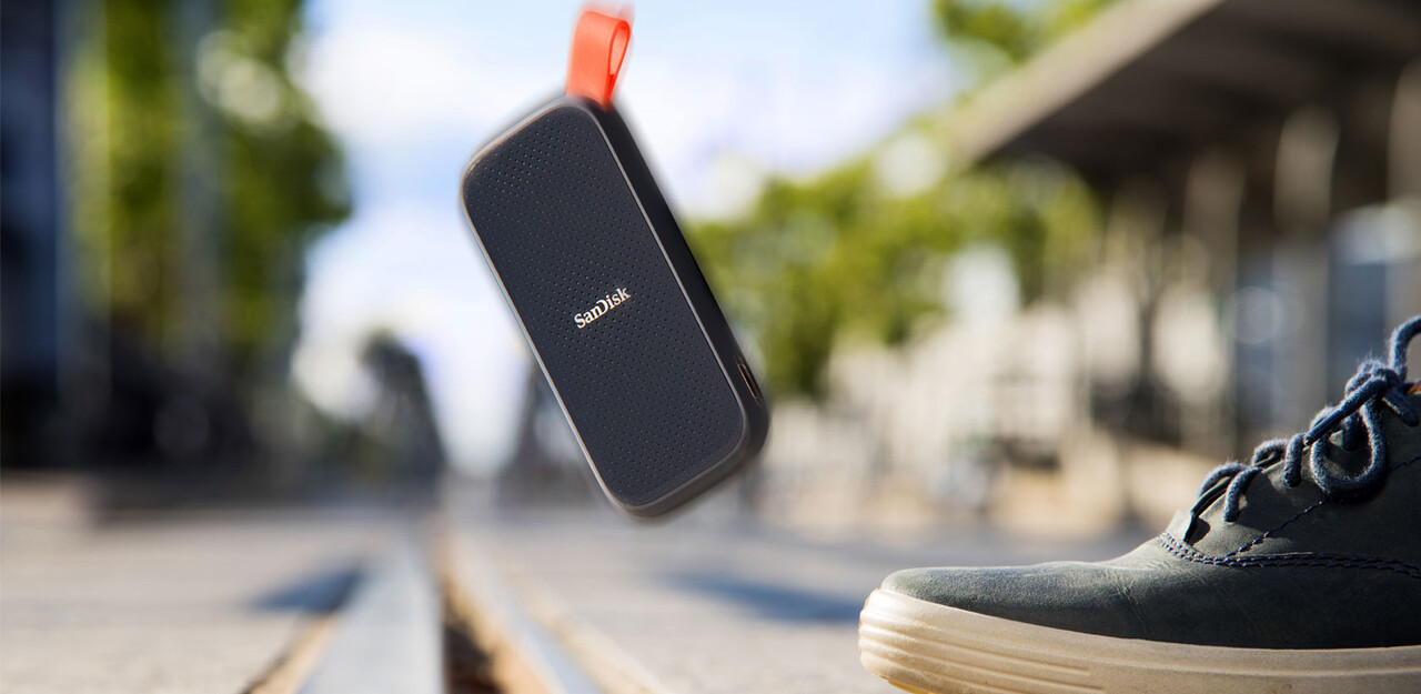 Eine schwarze und graue SanDisk externe Festplatte in der Luft, mit einem Schuh darunter.