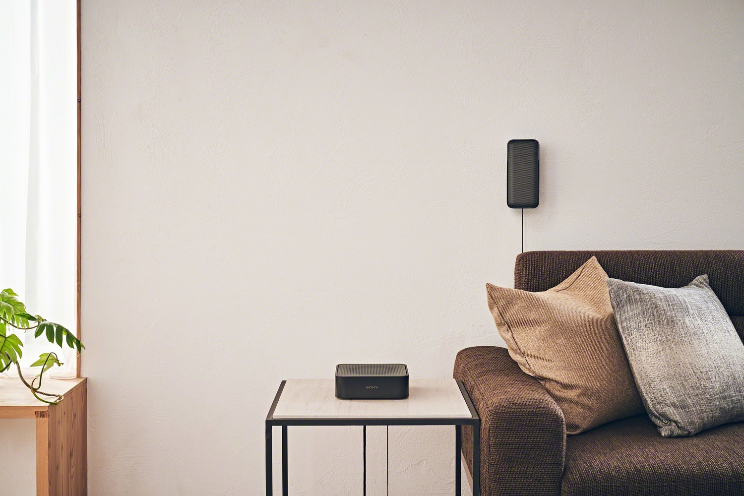 Altavoz negro en mesa, sofá con almohadas y altavoz montado en pared.