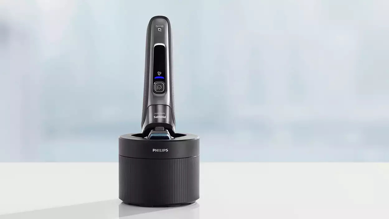 A gray and black electric shaver in its charging stand, positioned on a white surface.