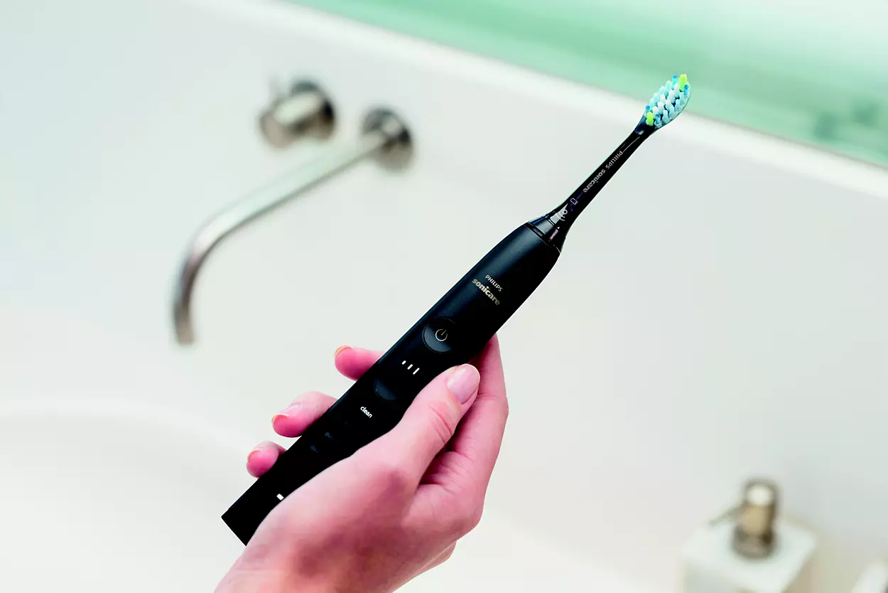 Main d'une personne tenant une brosse à dents électrique noire près d'un évier.