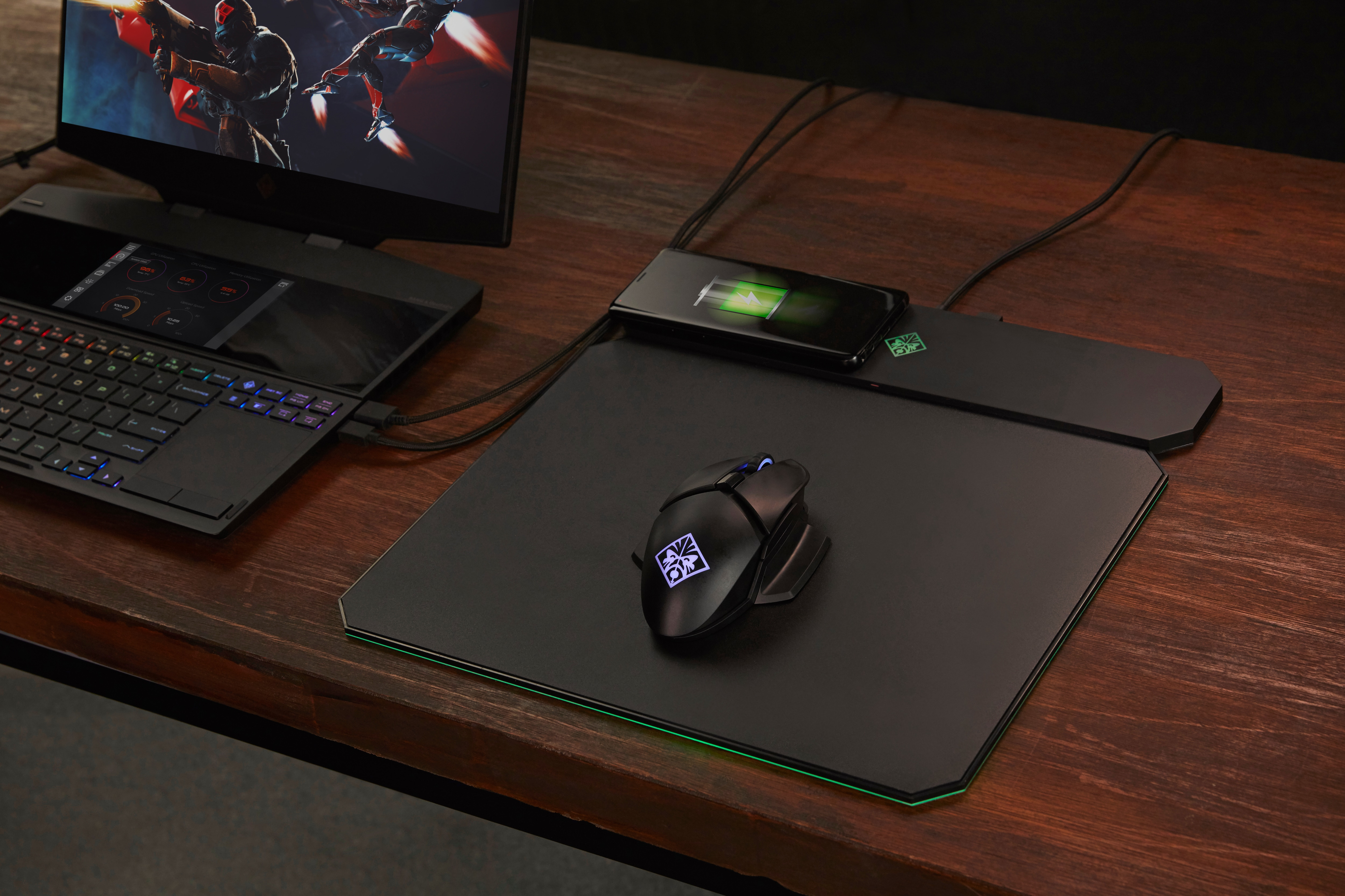 Een gaming laptop met muis en telefoon op een houten bureau.