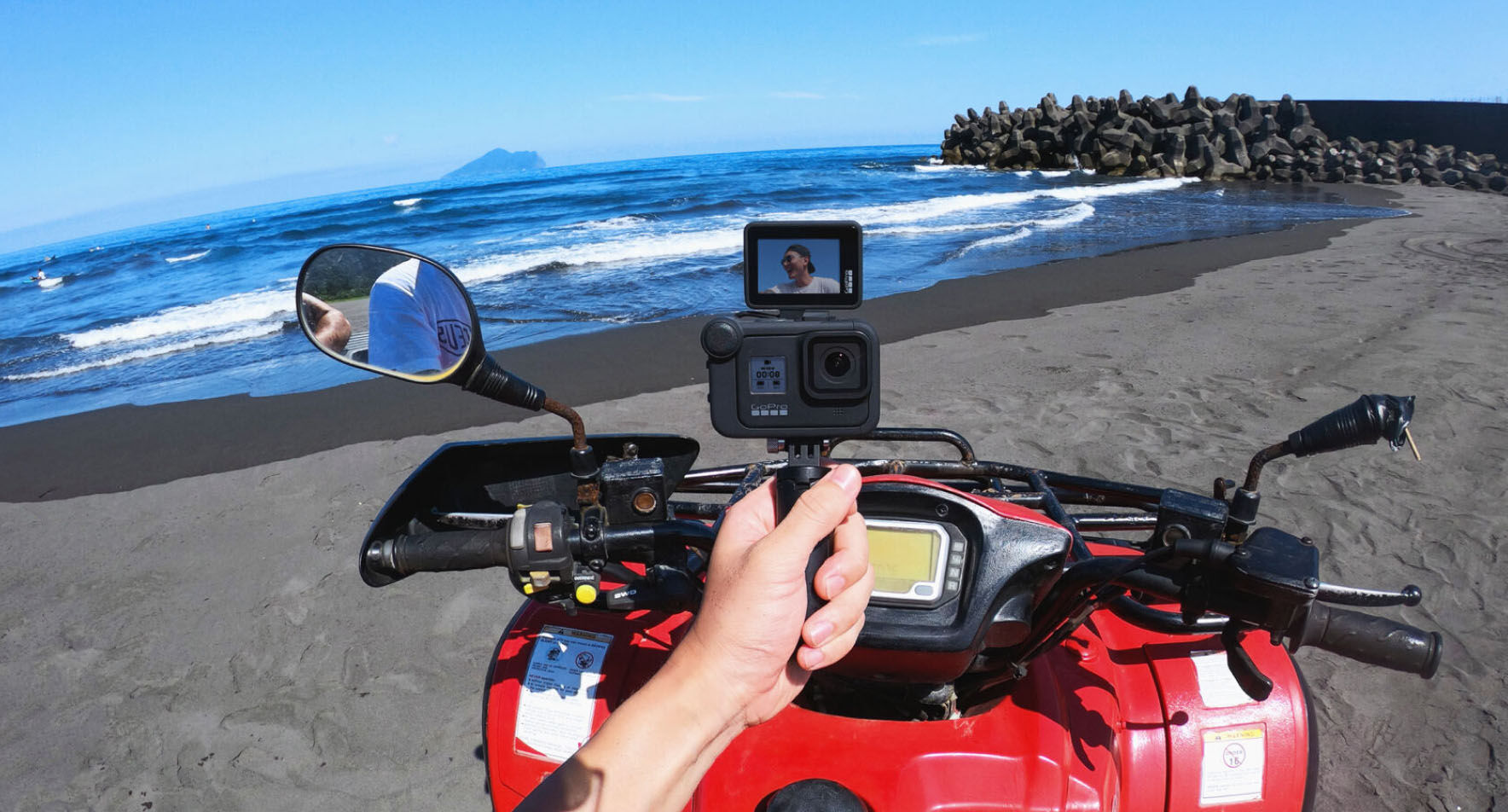 Személy GoPro-val filmez egy ATV-n a strandon. A háttérben a tenger és az ég látható.