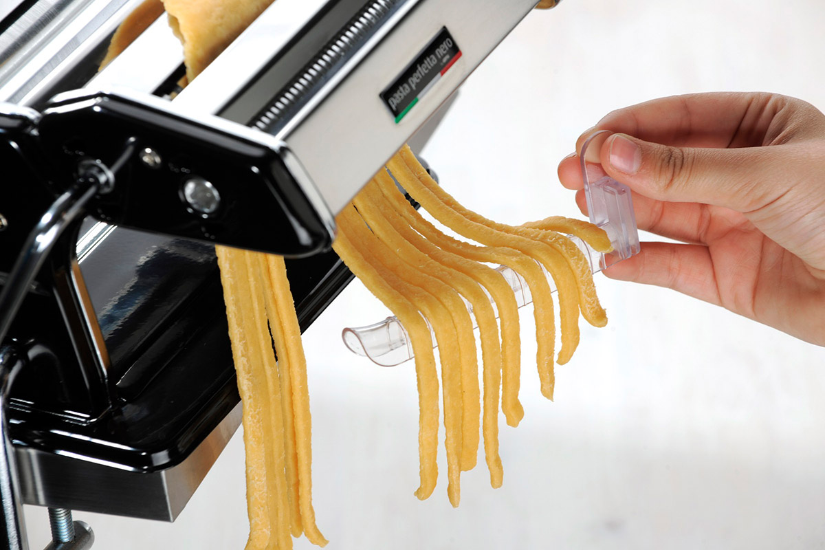 Pastamaschine, die frische Pasta extrudiert, Hand, die einen Schneider hält.