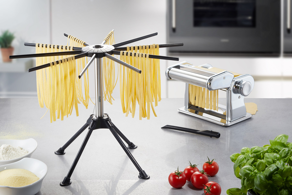 Nudeltrockner mit frischen Nudeln und Nudelmaschine auf einer Arbeitsplatte. Zutaten.