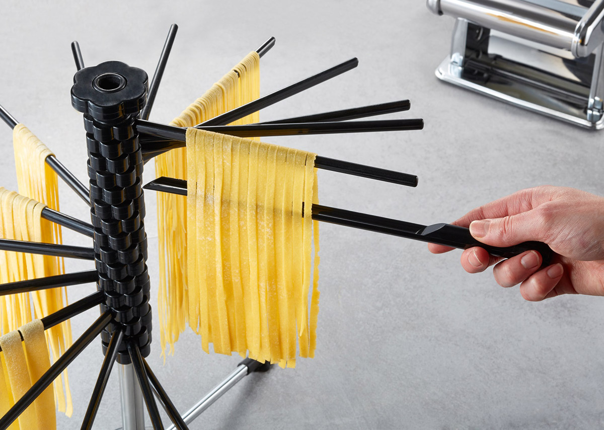 Nudeltrockner mit frischer Pasta und einer Hand, die einen Nudelstab hält.
