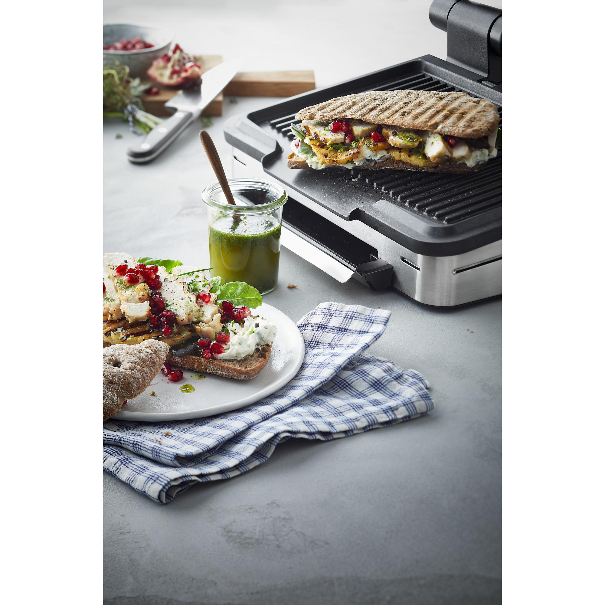 Gegrillte Sandwiches, Zutaten und ein Grill. Ein Sandwich liegt auf dem Grill, ein weiteres auf einem Teller.