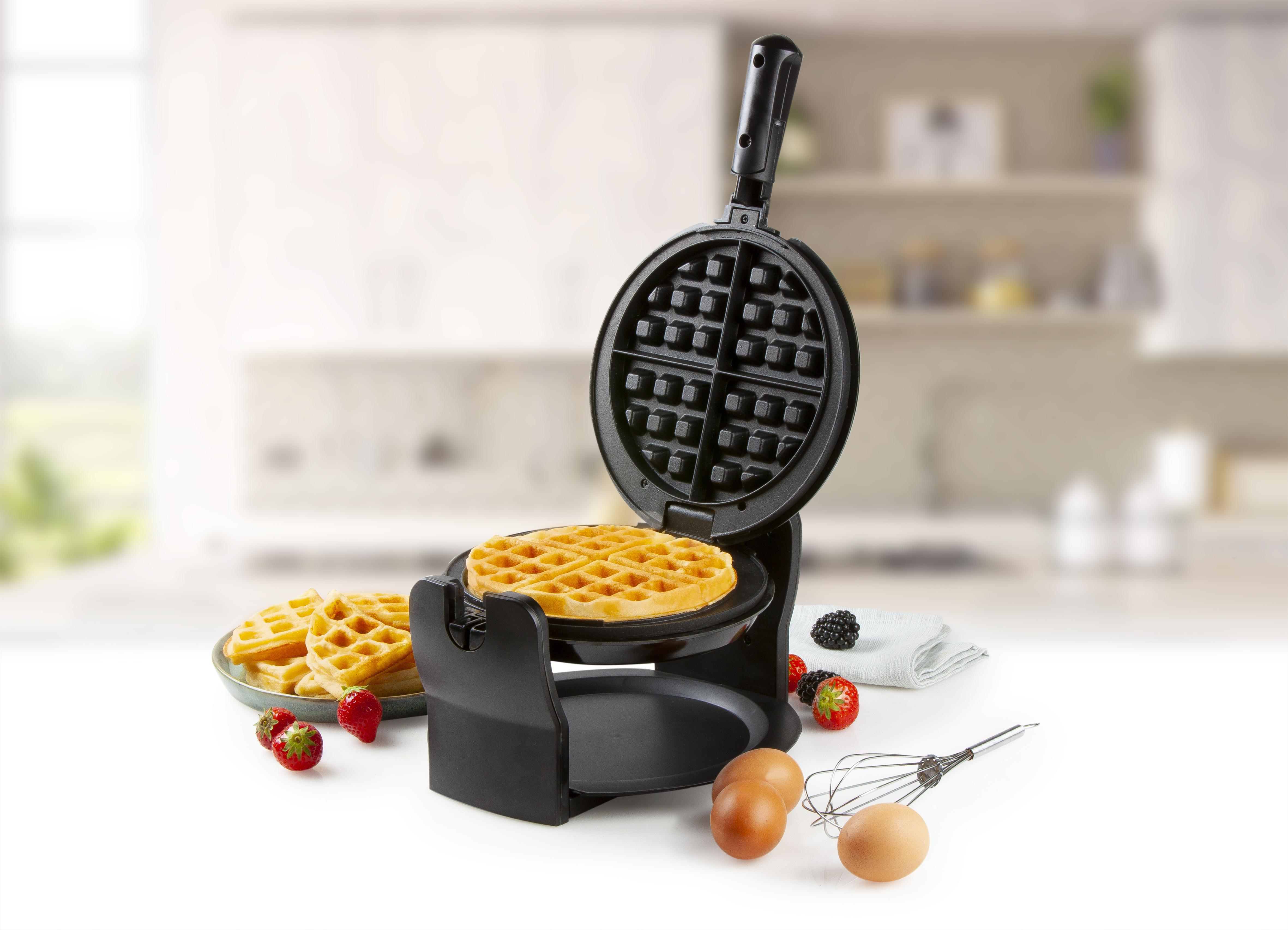 Waffeleisen geöffnet mit Waffel, Erdbeeren, Brombeeren, Eiern und Schneebesen auf dem Tisch.