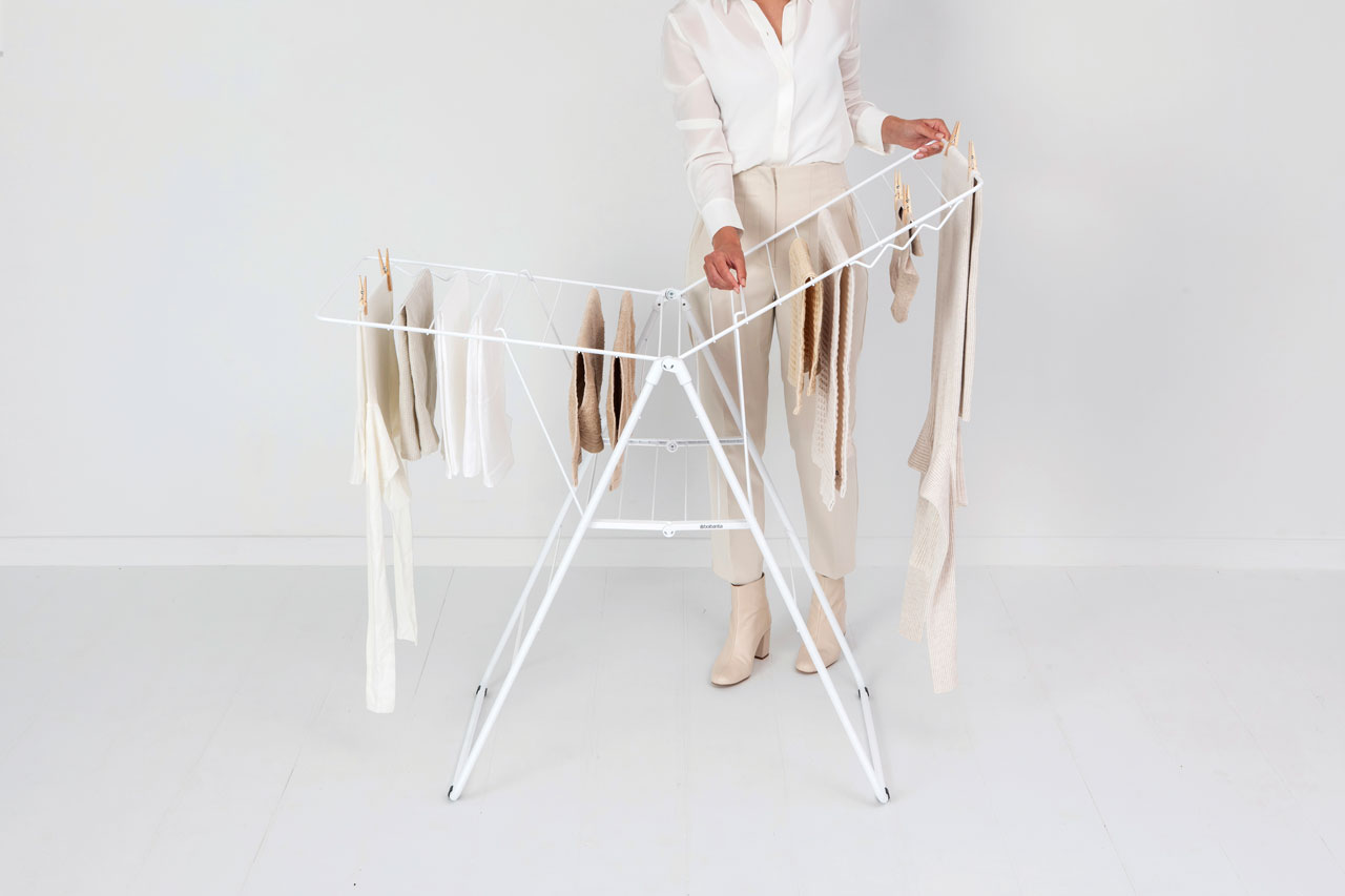 Une femme accroche du linge sur un étendoir blanc. Les vêtements sont de couleurs claires.