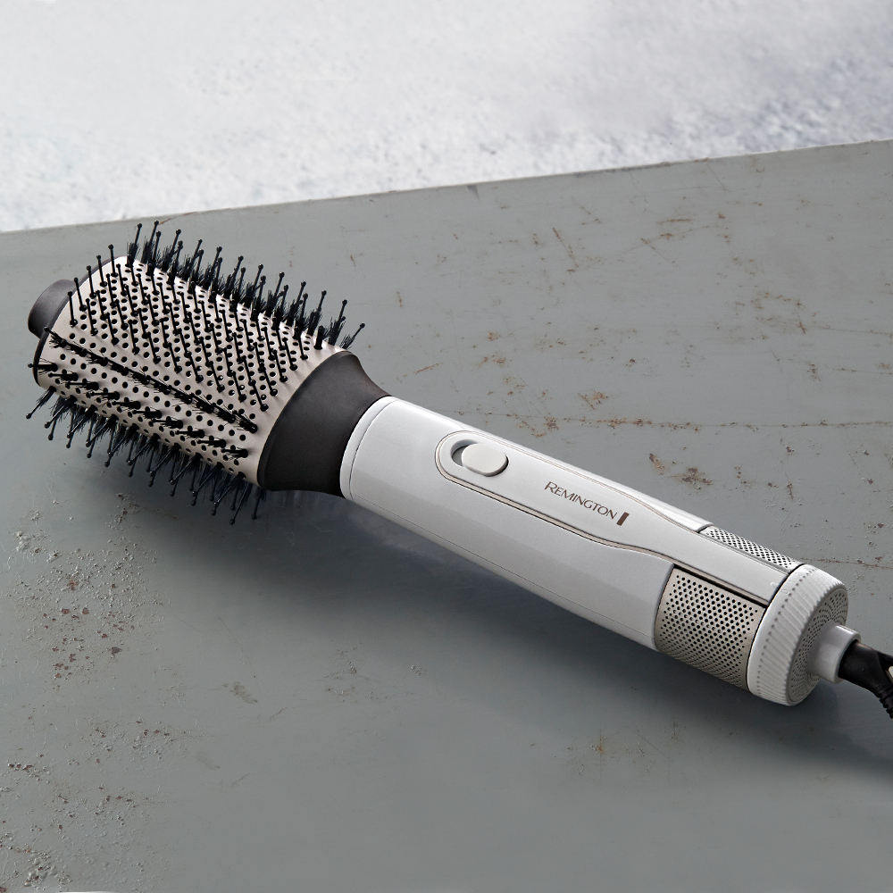 White and grey Remington hair styling brush on a grey surface. The brush has black bristles and white body.