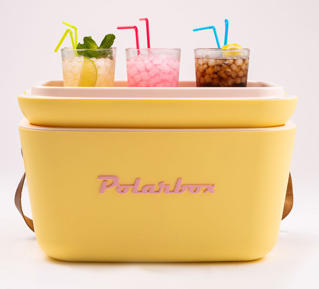 Glacière jaune avec boissons et pailles dessus. Texte rose 'Polarbox'. Fond blanc.