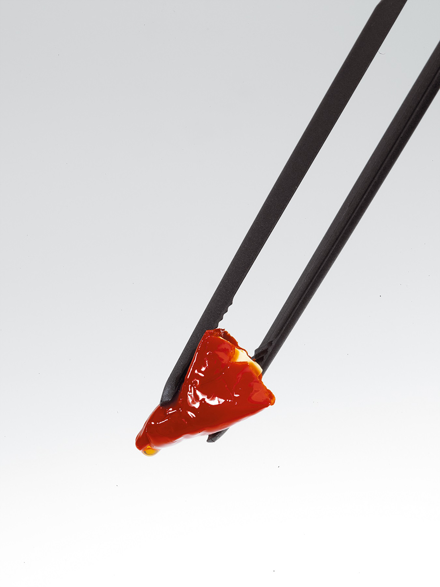 Essstäbchen halten ein Stück rotes Essen auf weißem Hintergrund.