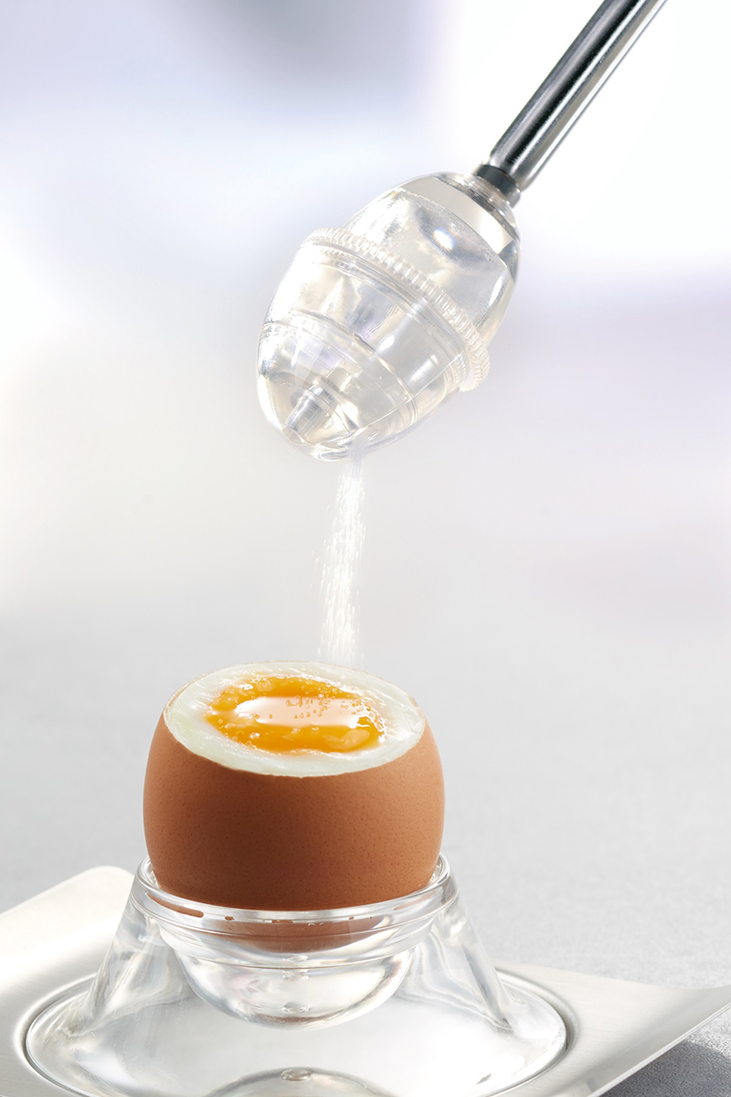 Ei in Eierbecher, weißer Schaum wird aus einem durchsichtigen Behälter gegossen.