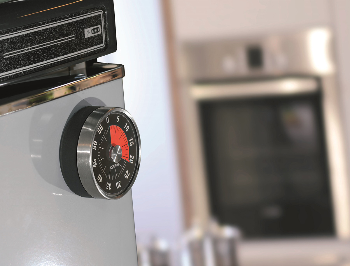 Küchenuhr an Kühlschrank. Edelstahl-Timer mit rotem Detail. Verschwommener Hintergrund.