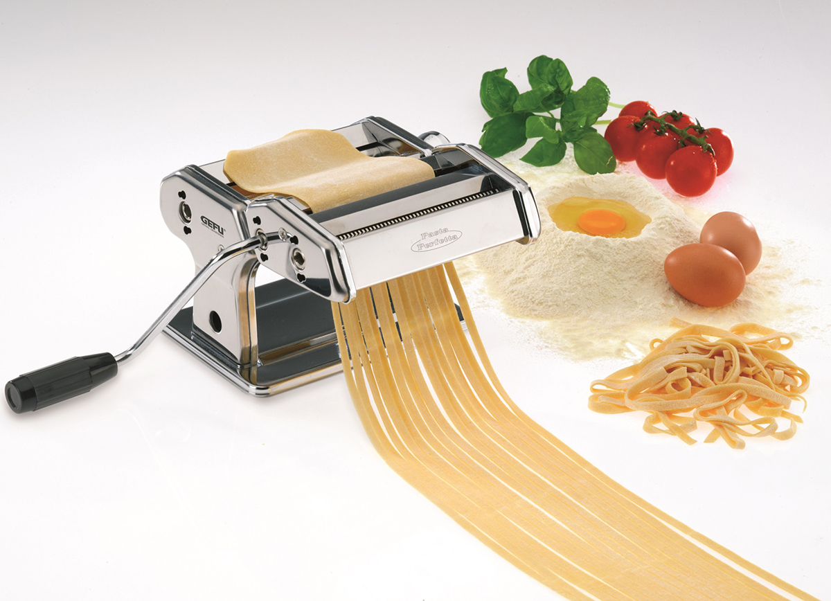 Pastamaker mit Teig, Bandnudeln, Mehl, Ei, Tomaten und Basilikumblättern.