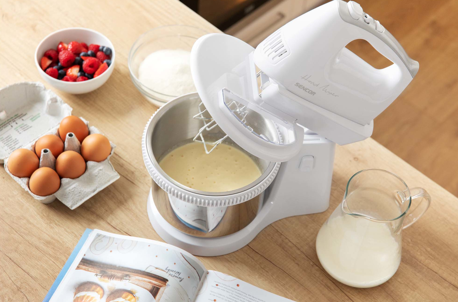 Fehér kézi mixer tálba, tojással, cukorral és bogyókkal.