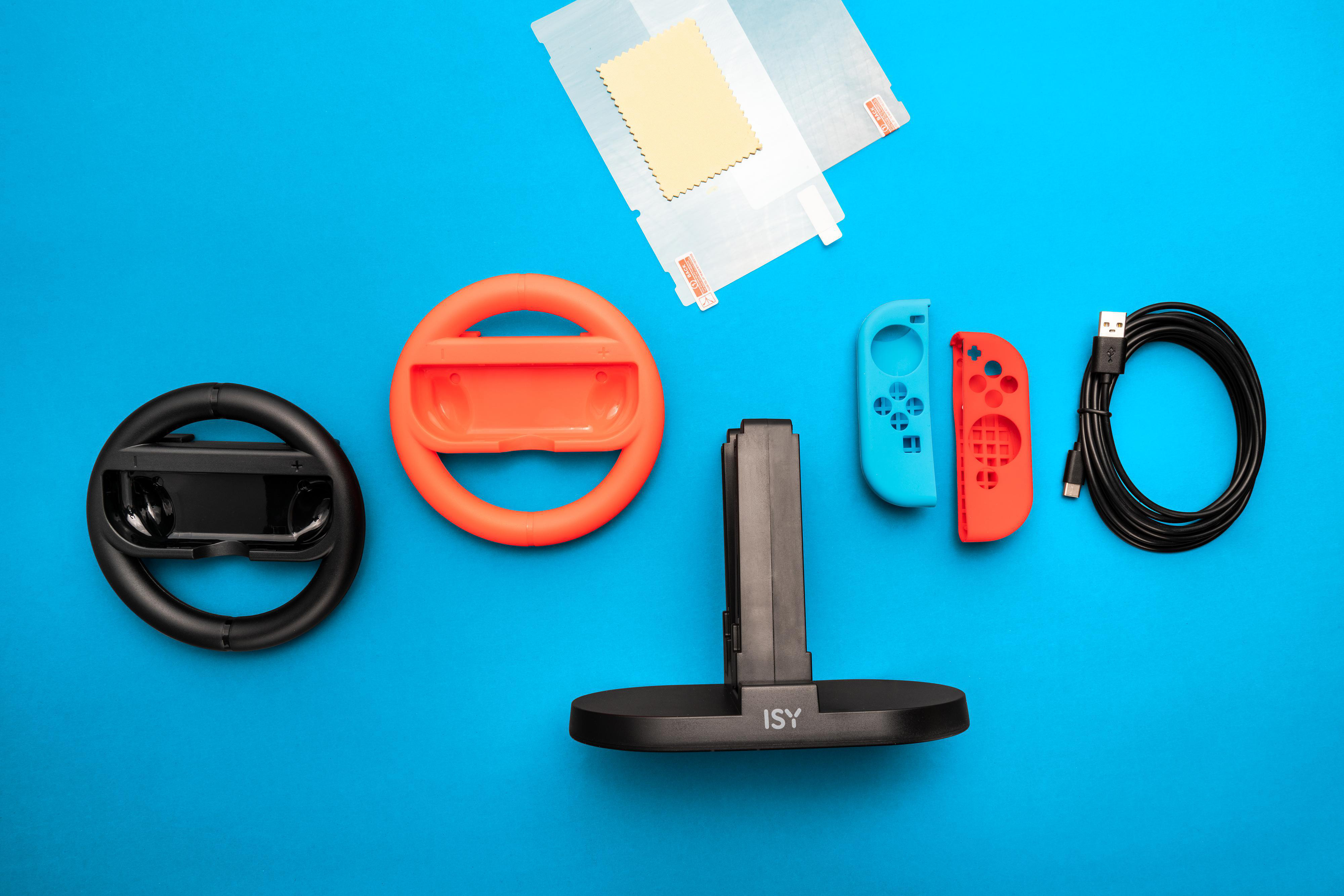 Gaming-Zubehör auf blauer Oberfläche: Lenkrad, Controller, Ladeständer und Kabel.