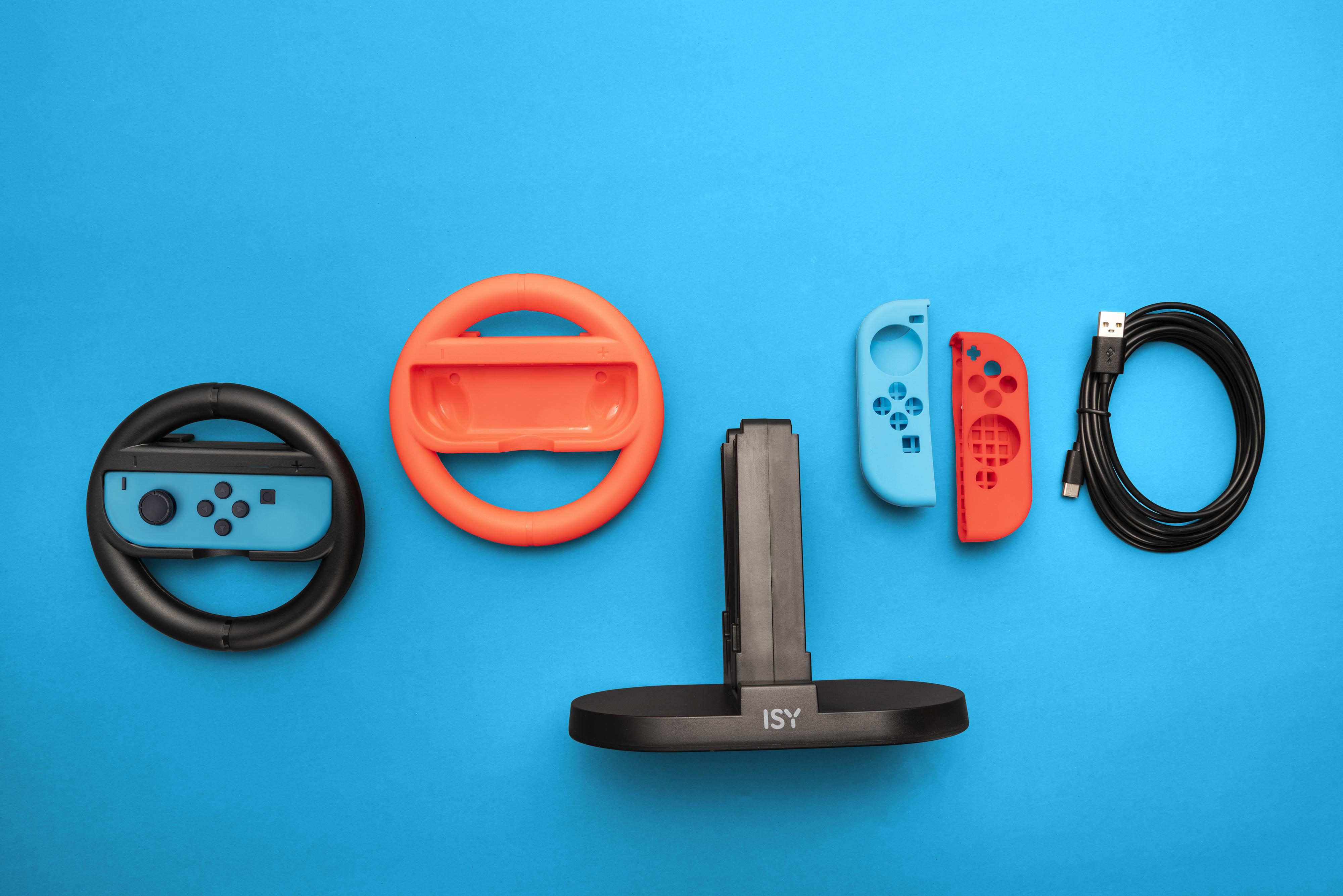 Gaming-Zubehör auf blauer Oberfläche. Enthält ein Lenkrad, Controller und einen Ladeständer.