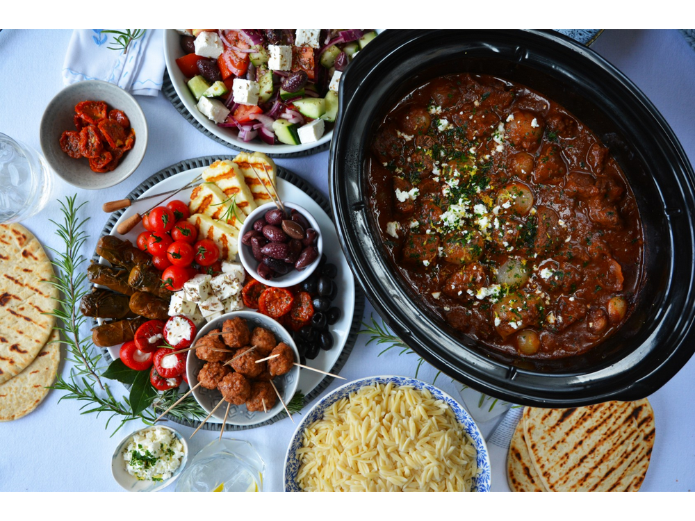 Vista aérea de una mesa con comida griega. Incluye tomates, aceitunas y varios platos.