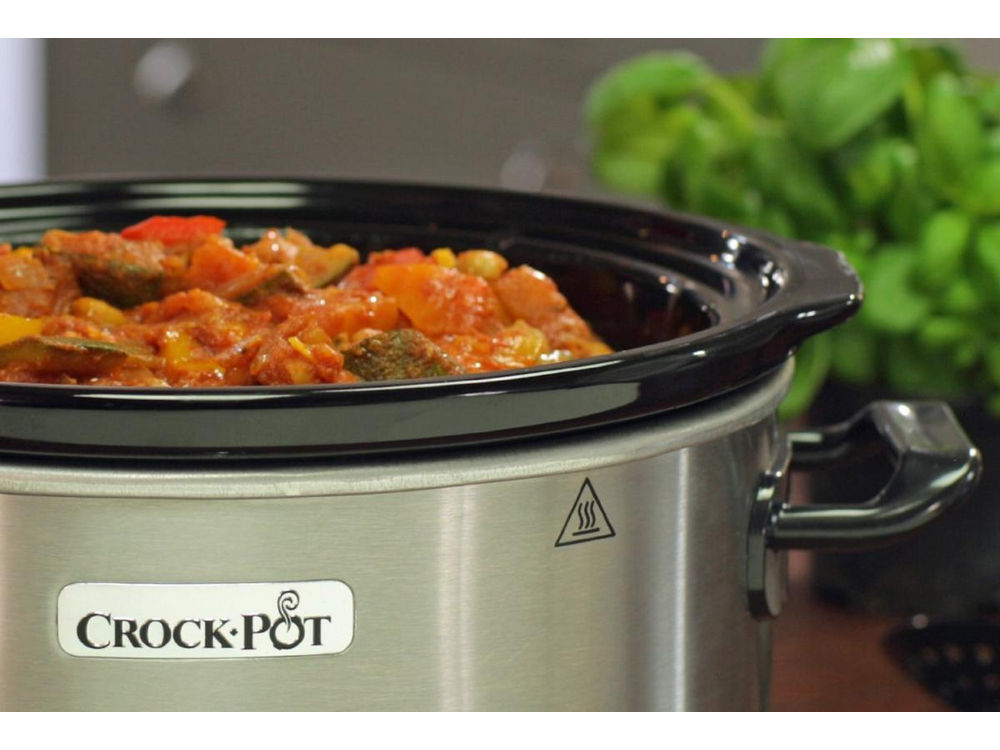 Crock-Pot con estofado. Hierbas verdes en el fondo.