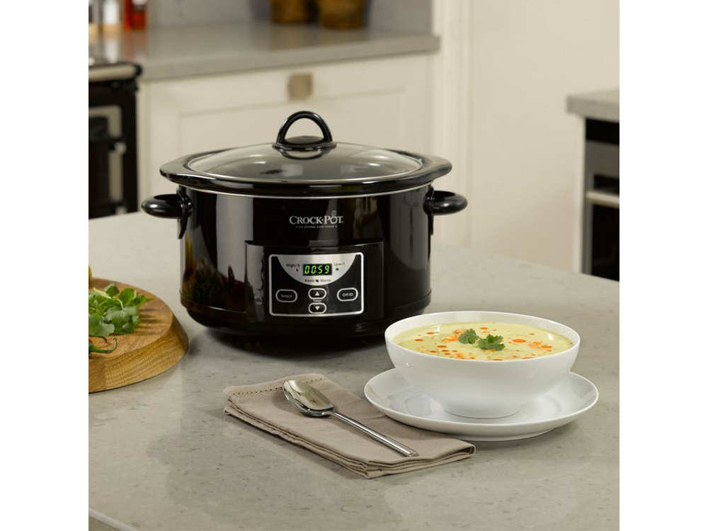 Crock-Pot negro en la encimera, tazón de sopa, cuchara y servilleta. Fondo de cocina.