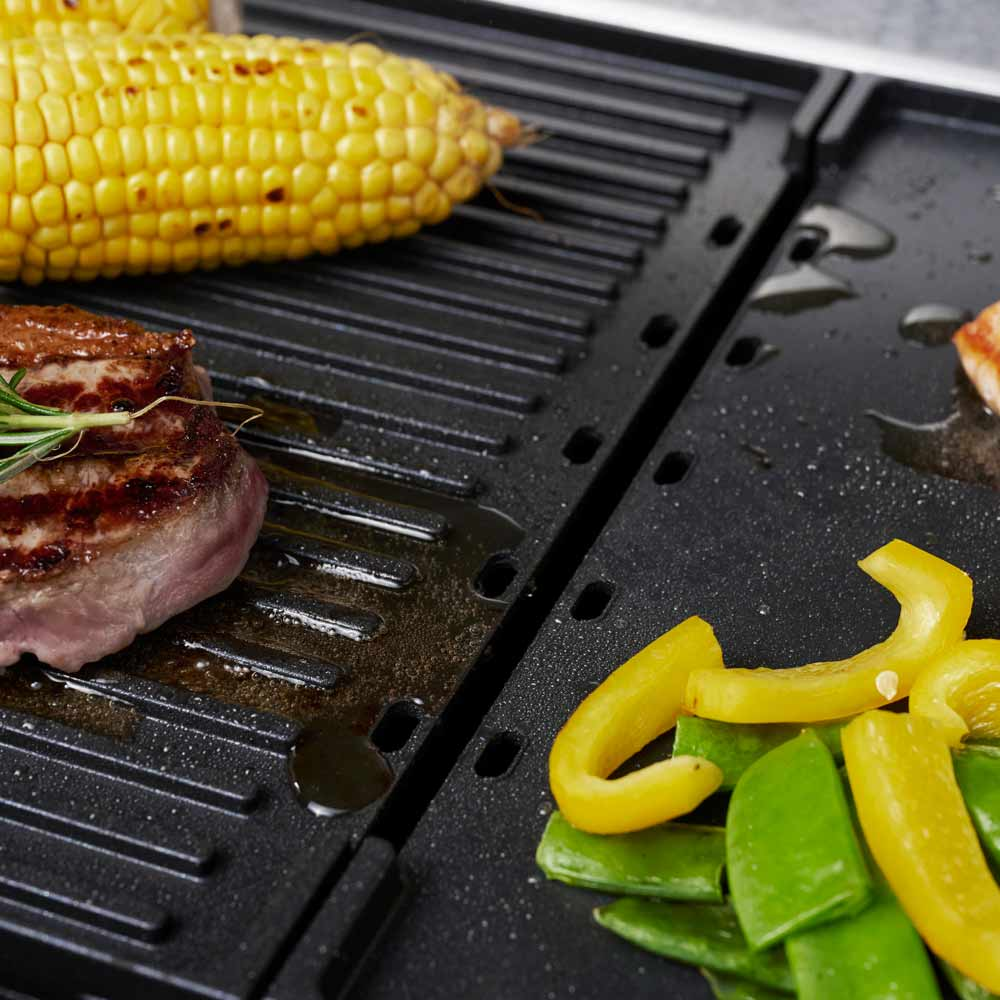 Gegrilltes Essen auf einem schwarzen Grill. Steak, Mais und Gemüse sichtbar.