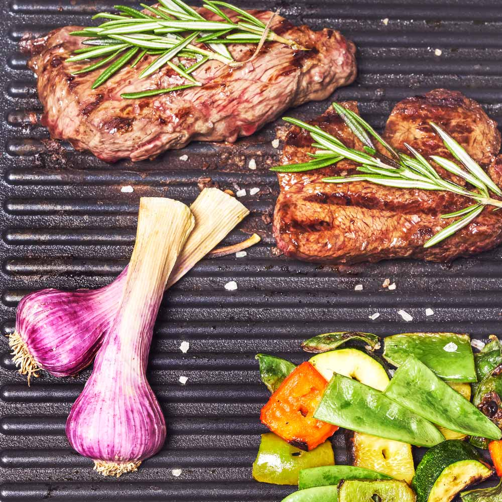 Gegrillte Steaks mit Rosmarin und Knoblauch auf einem Grill. Gemüse auch auf dem Grill.