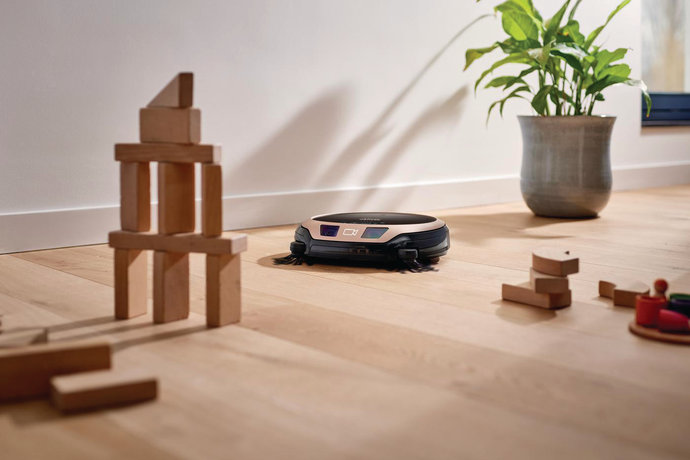Roboter-Staubsauger auf Holzboden mit Blöcken und Pflanze.