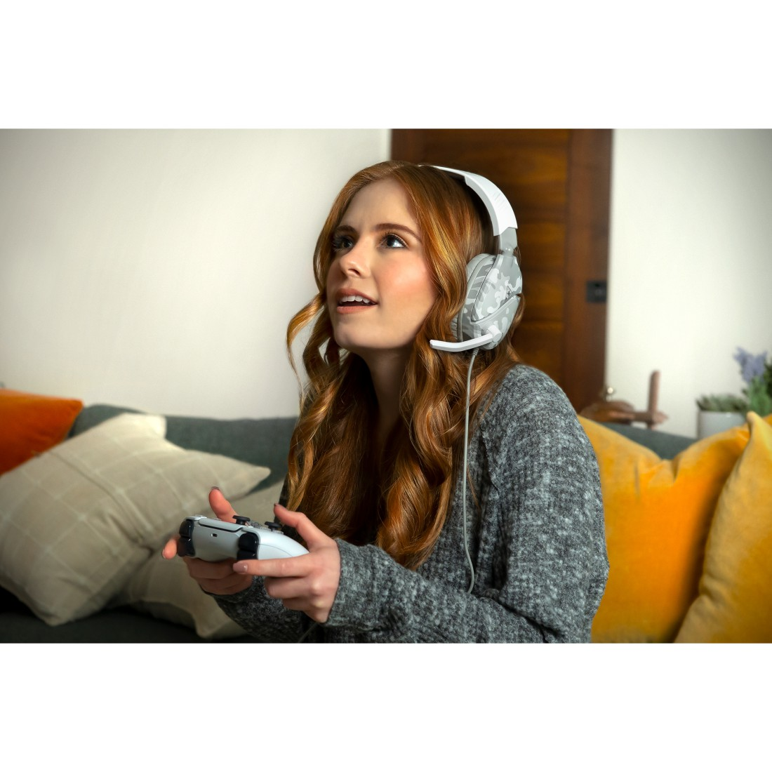 Eine junge Frau mit roten Haaren trägt einen grauen Pullover und Kopfhörer und spielt Videospiele.
