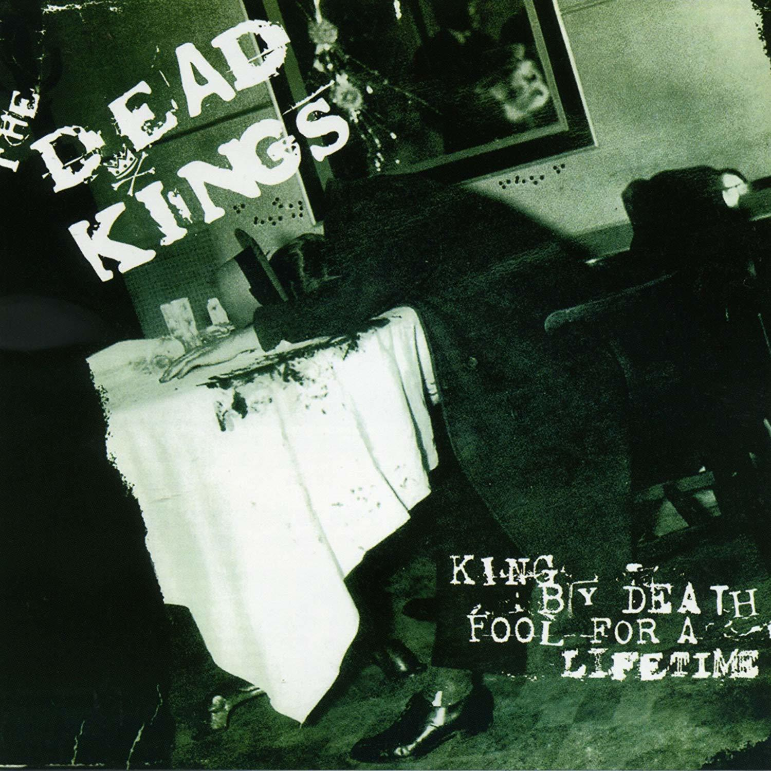 Albumcover mit Text, einem Tisch und einer Person im Schatten, ein Bild an der Wand.