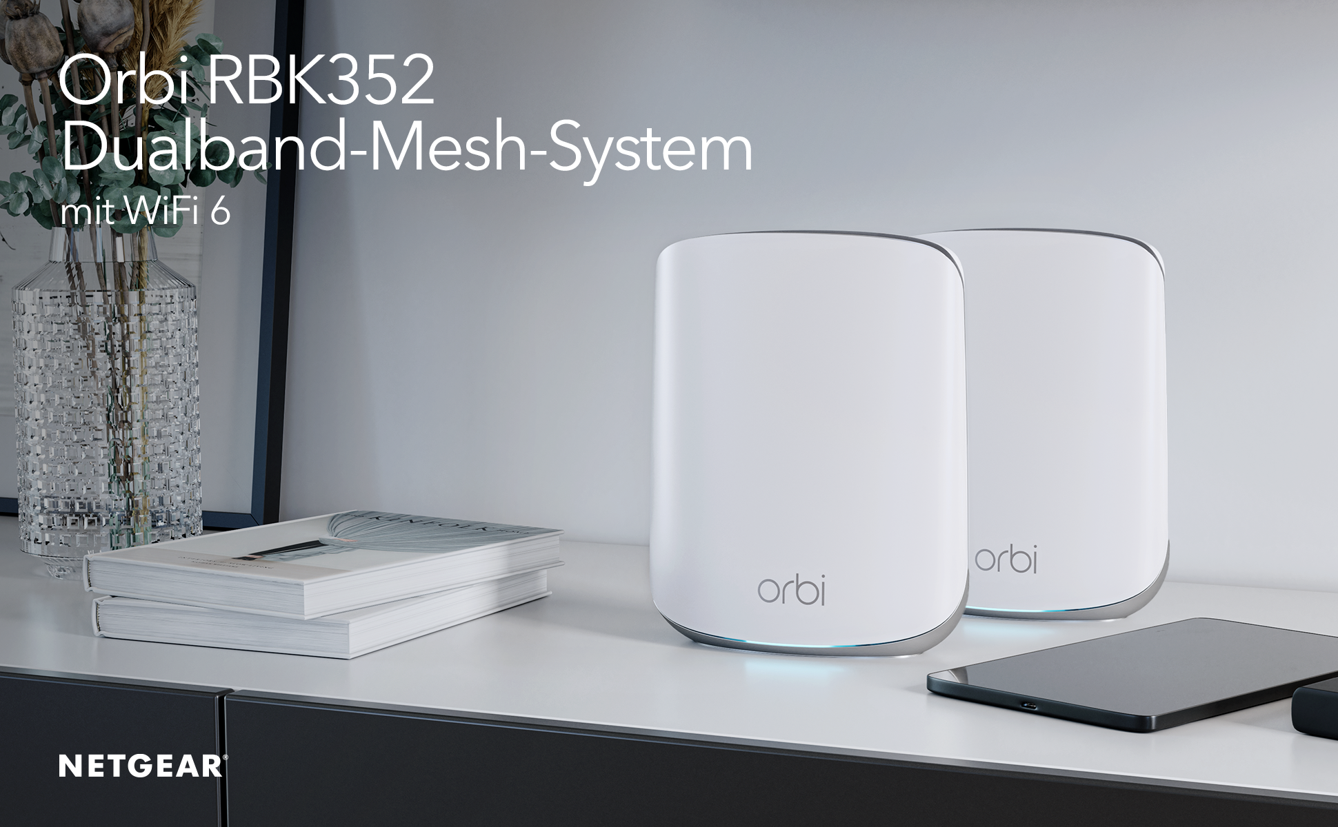 Zwei weiße Orbi WLAN-Geräte auf einem Regal. Ein Buch und ein Tablet befinden sich in der Nähe. NETGEAR-Logo sichtbar.