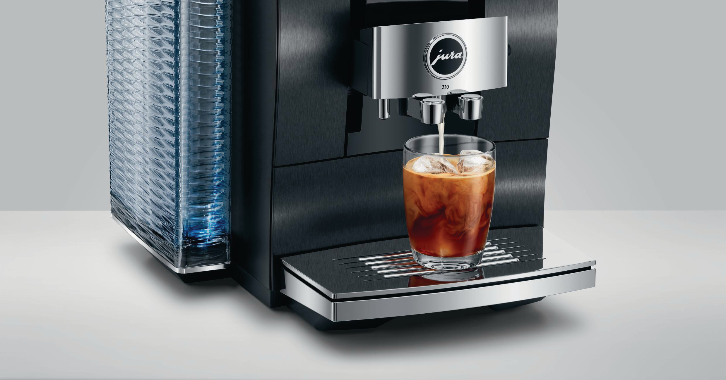 Schwarze und silberne Jura Z10 Kaffeemaschine, die Eiskaffee in ein Glas ausgibt, links ein Stapel Becher.