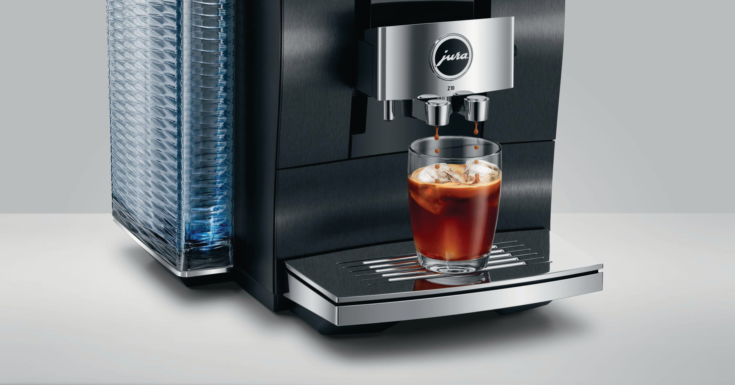Eine schwarze Jura Kaffeemaschine mit Kaffee, der in ein Glas mit Eis gegossen wird. Links ein Stapel Becher.