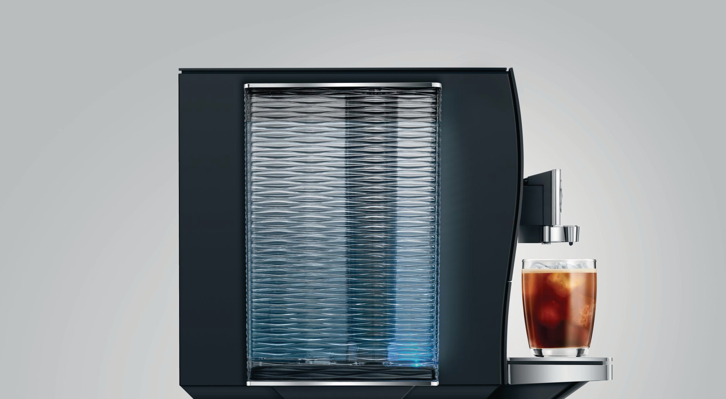 Eine schwarze Kaffeemaschine mit einem Glas Eiskaffee. Sie steht auf einem hellgrauen Hintergrund.
