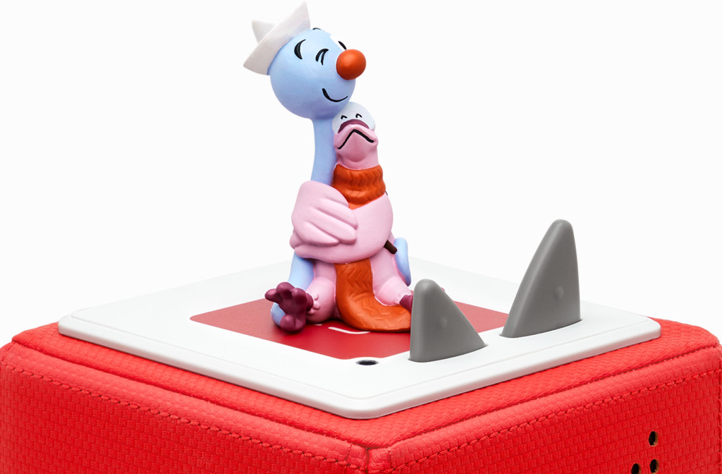 Eine Spielfigur eines blauen Charakters, der einen rosa umarmt, auf einer roten Box mit grauen Haifischflossen.