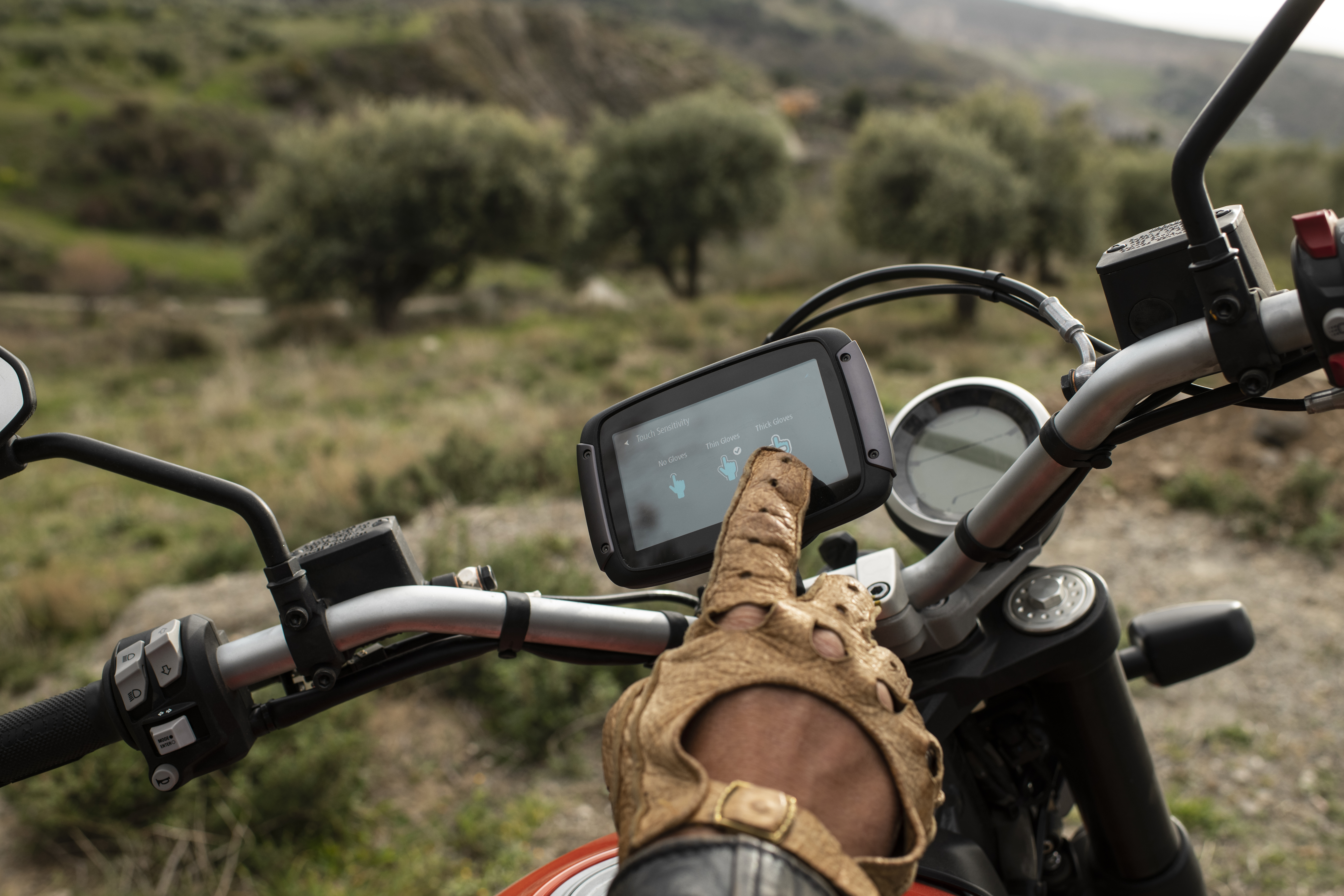 Eine Hand in einem Lederhandschuh bedient im Freien den Navigationsbildschirm eines Motorrads.