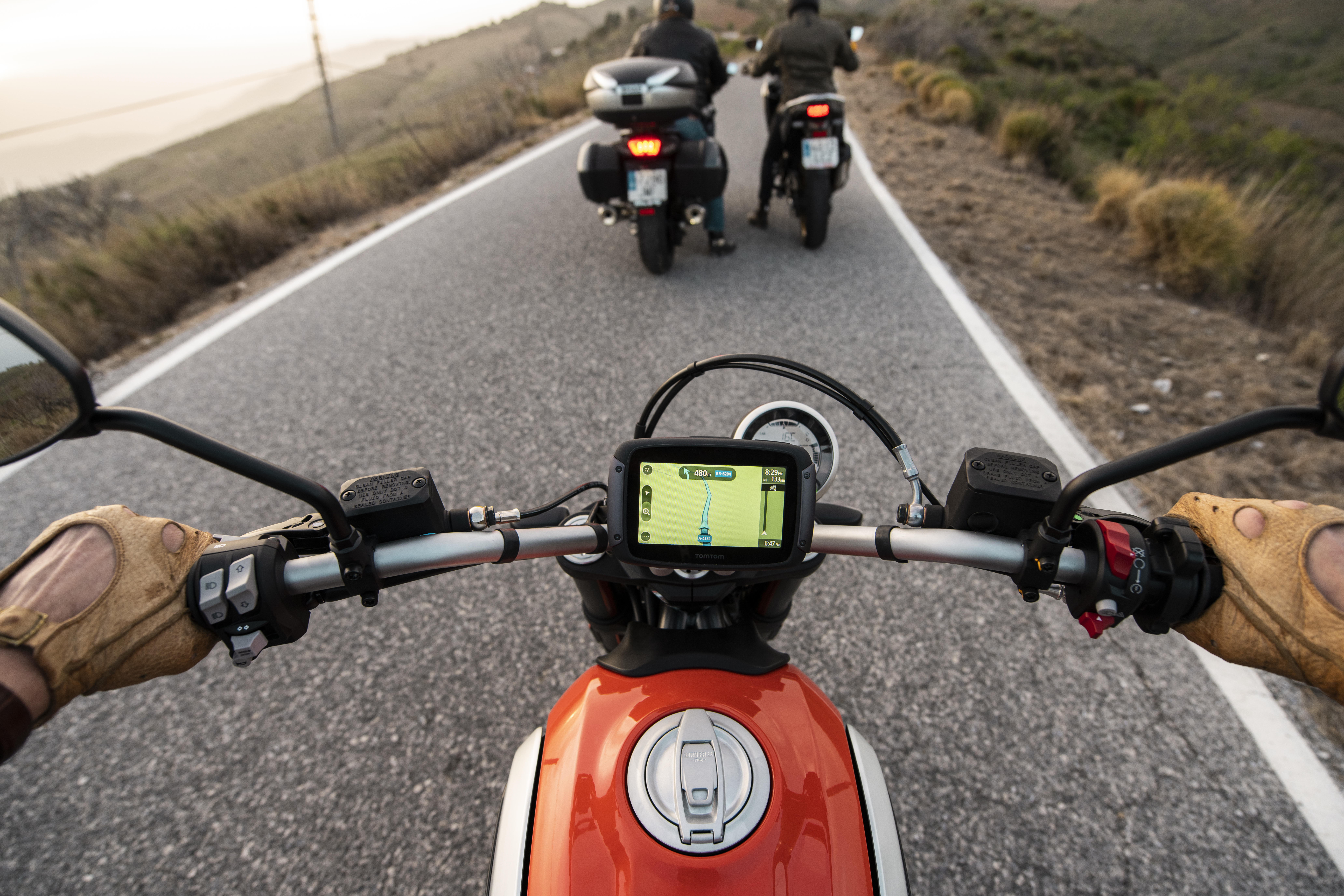 Eine Ego-Perspektive einer Motorradfahrt. Die Hände des Fahrers sind sichtbar, ein weiteres Motorrad voraus.