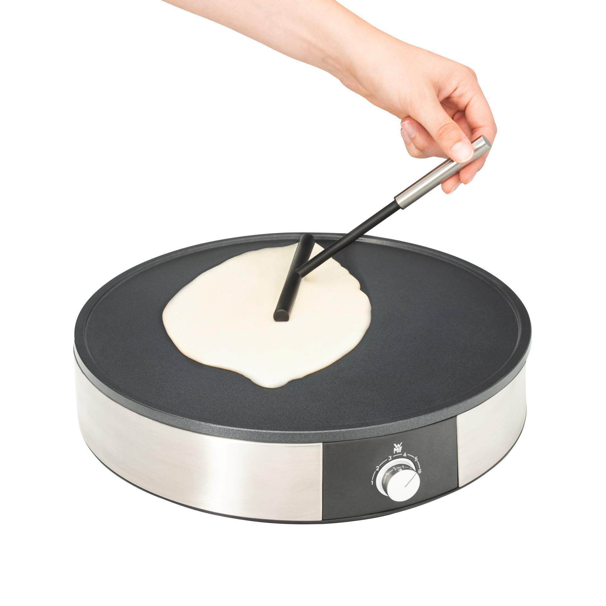Eine Person macht einen Pfannkuchen auf einer Grillplatte. Ein Spatel wird zum Verteilen des Teigs verwendet.