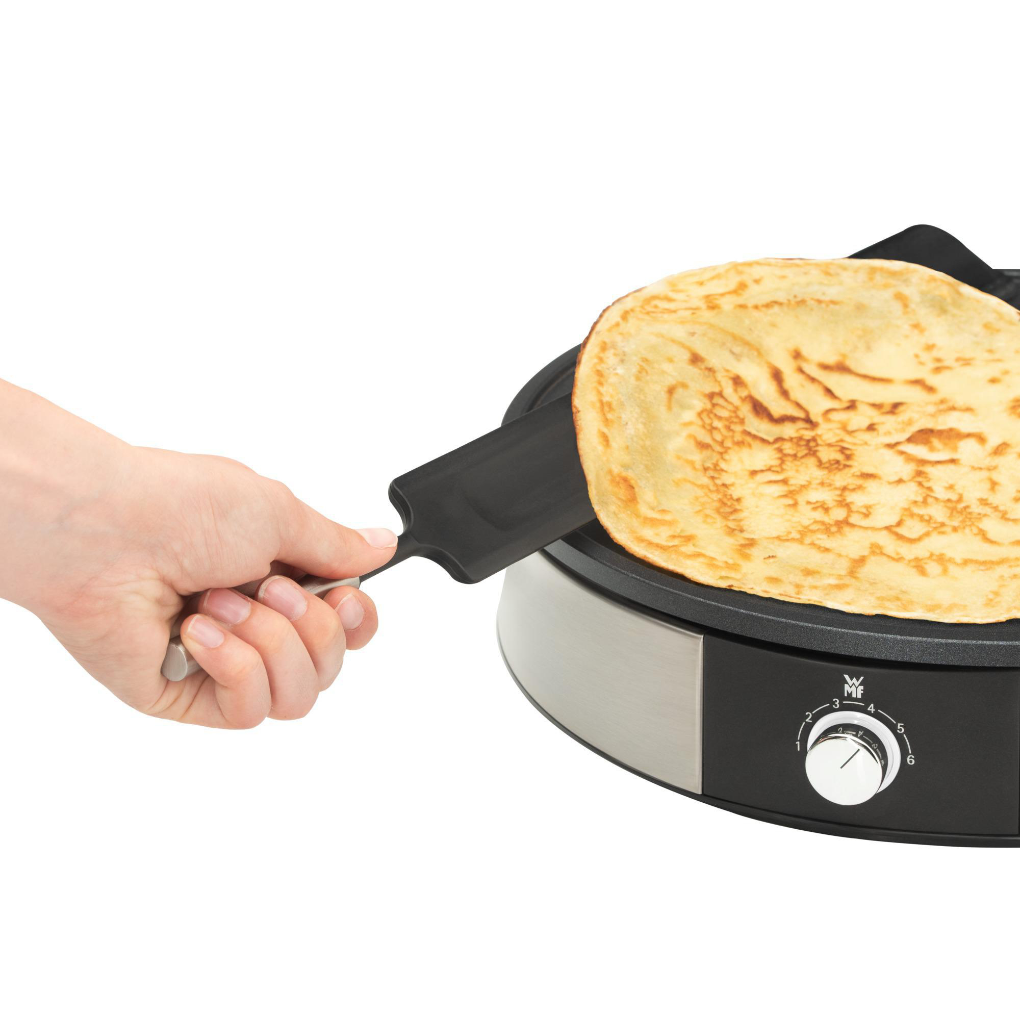 Hand, die einen Spatel benutzt, um einen Pfannkuchen auf einer schwarzen Grillplatte zu wenden.