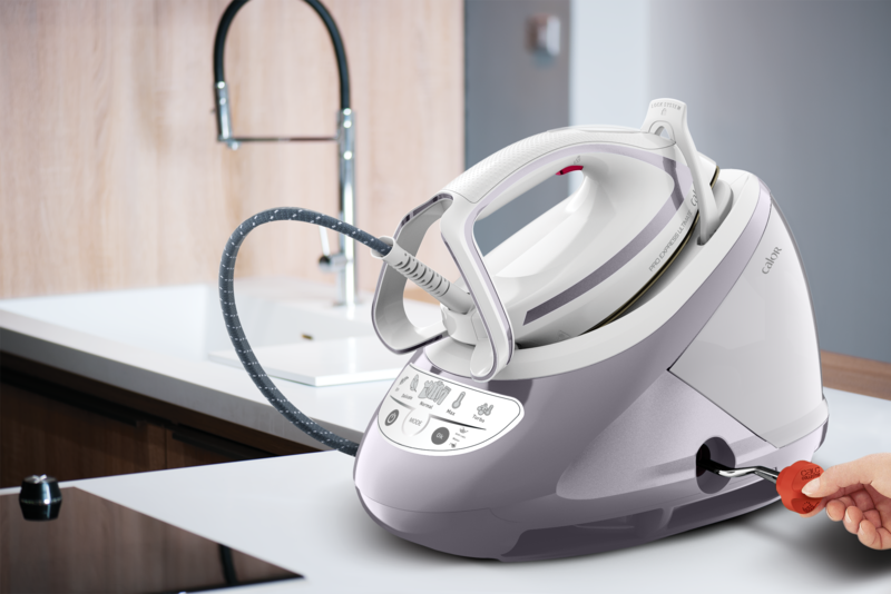 Ironing station with iron on a white surface. A hand inserts a red plug.  The word 'Calor' is visible.