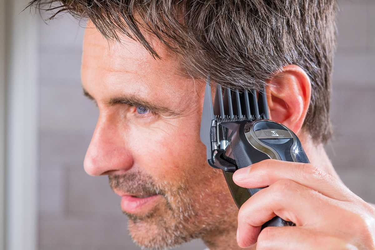 Man cutting his hair with clippers, side view, focus on the hair and clippers.