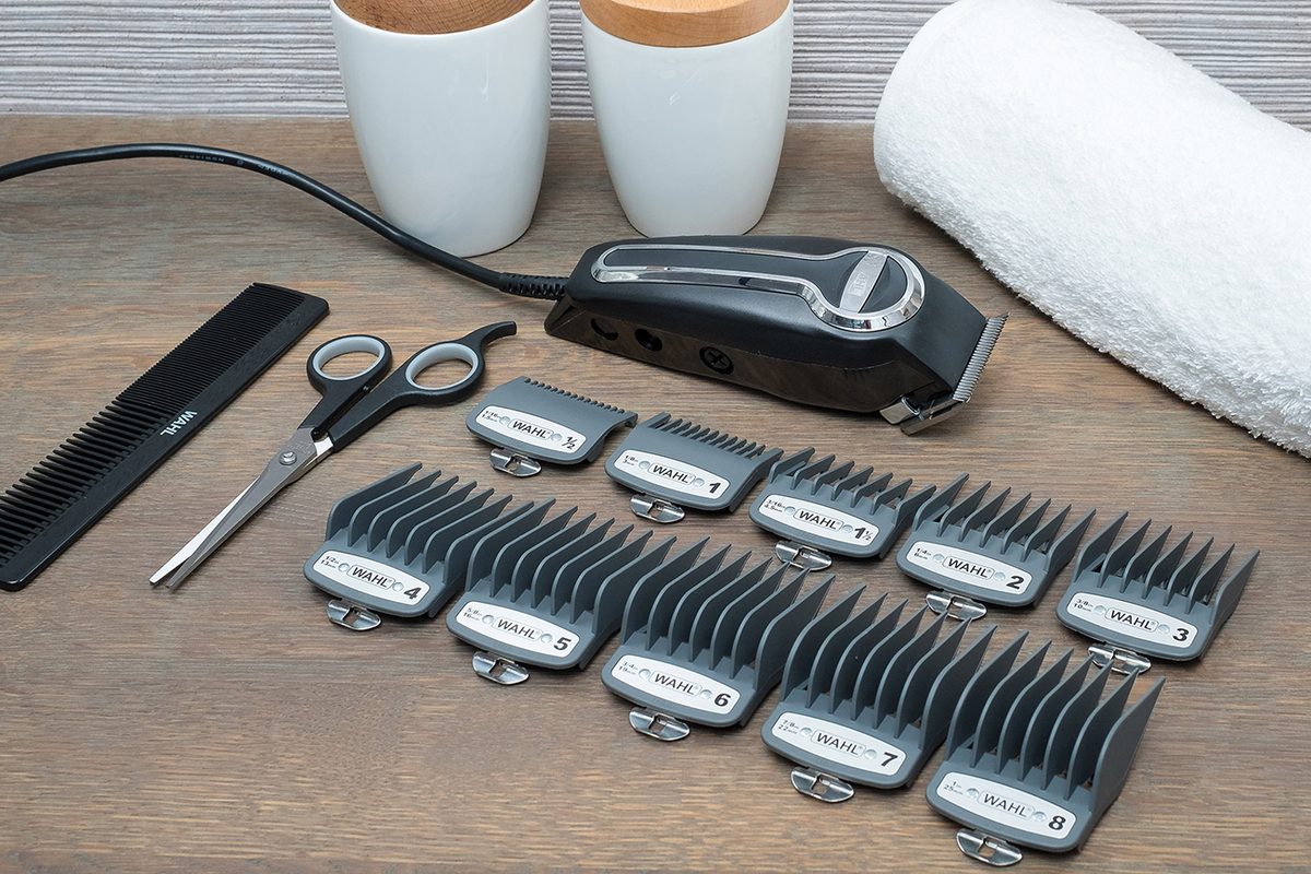 Hair clippers, comb, scissors, and clipper guards are arranged on a wooden surface, ready for use.
