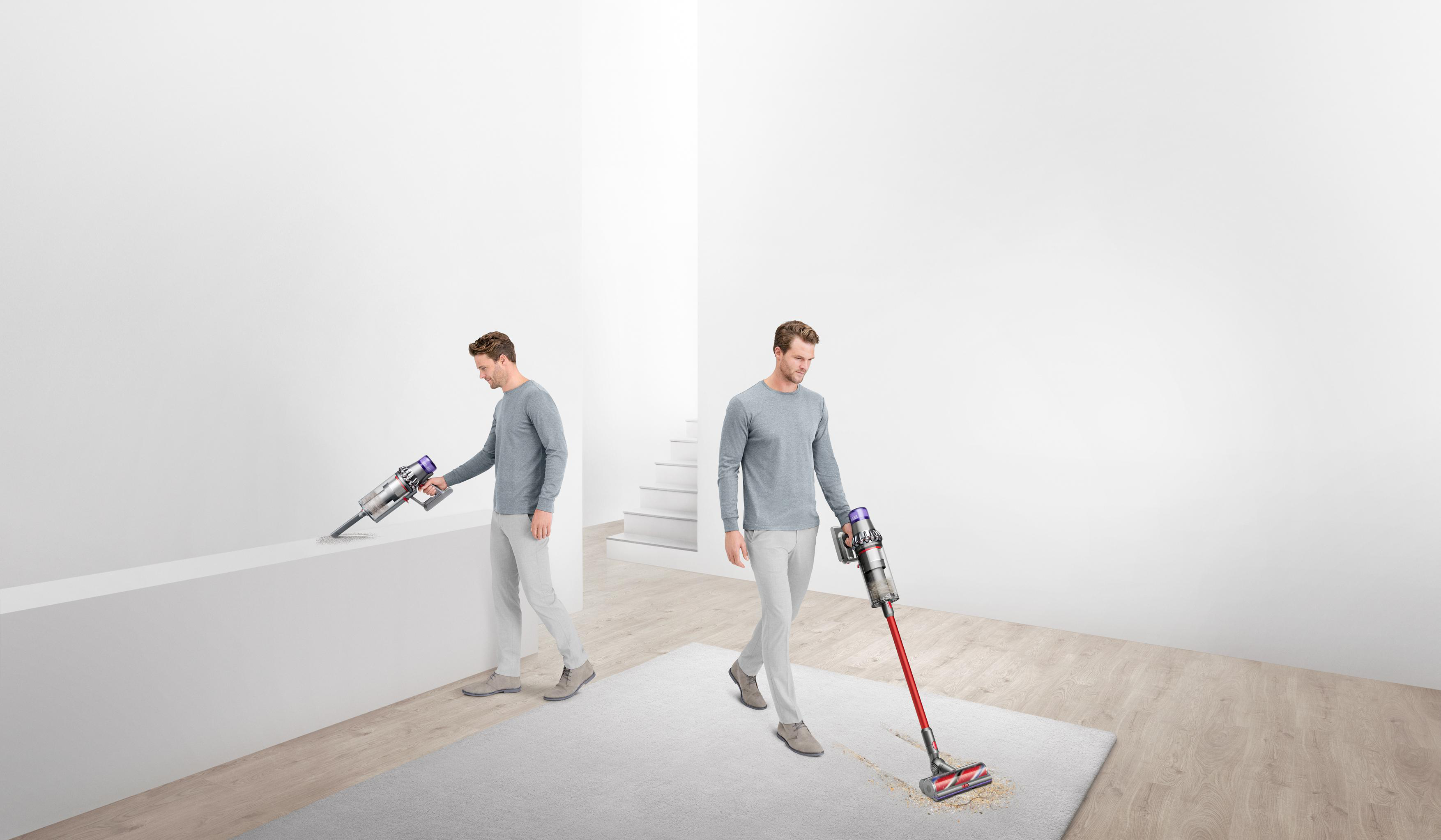 Ein Mann saugt einen Teppich mit einem roten und grauen Akku-Staubsauger. Ein anderer Mann saugt eine Wand. Der Hintergrund ist weiß.