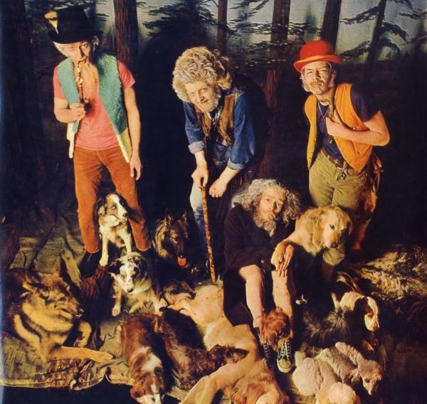 Eine Gruppe Männer in Kostümen mit Hunden, posierend vor bemalter Waldkulisse.