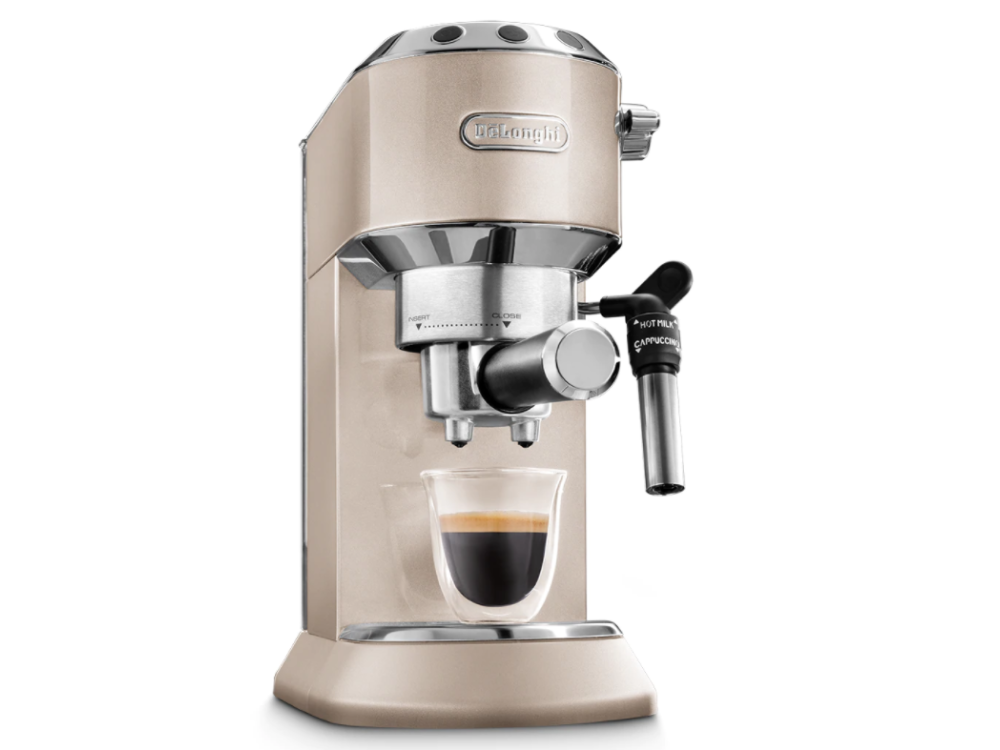 Cafetera espresso beige con un vaso de espresso. Cuenta con una varilla de vapor y controles.
