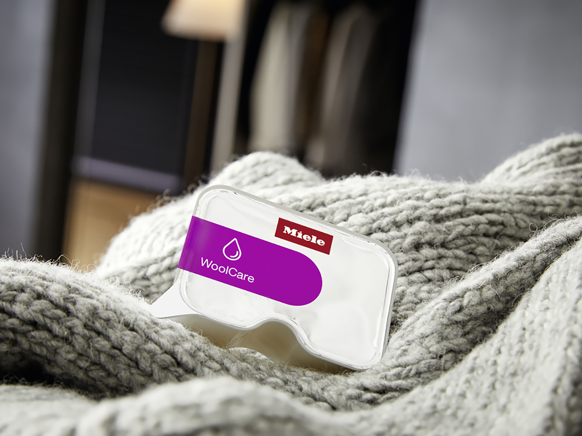 White and purple Miele WoolCare laundry detergent pod on a grey knitted sweater.