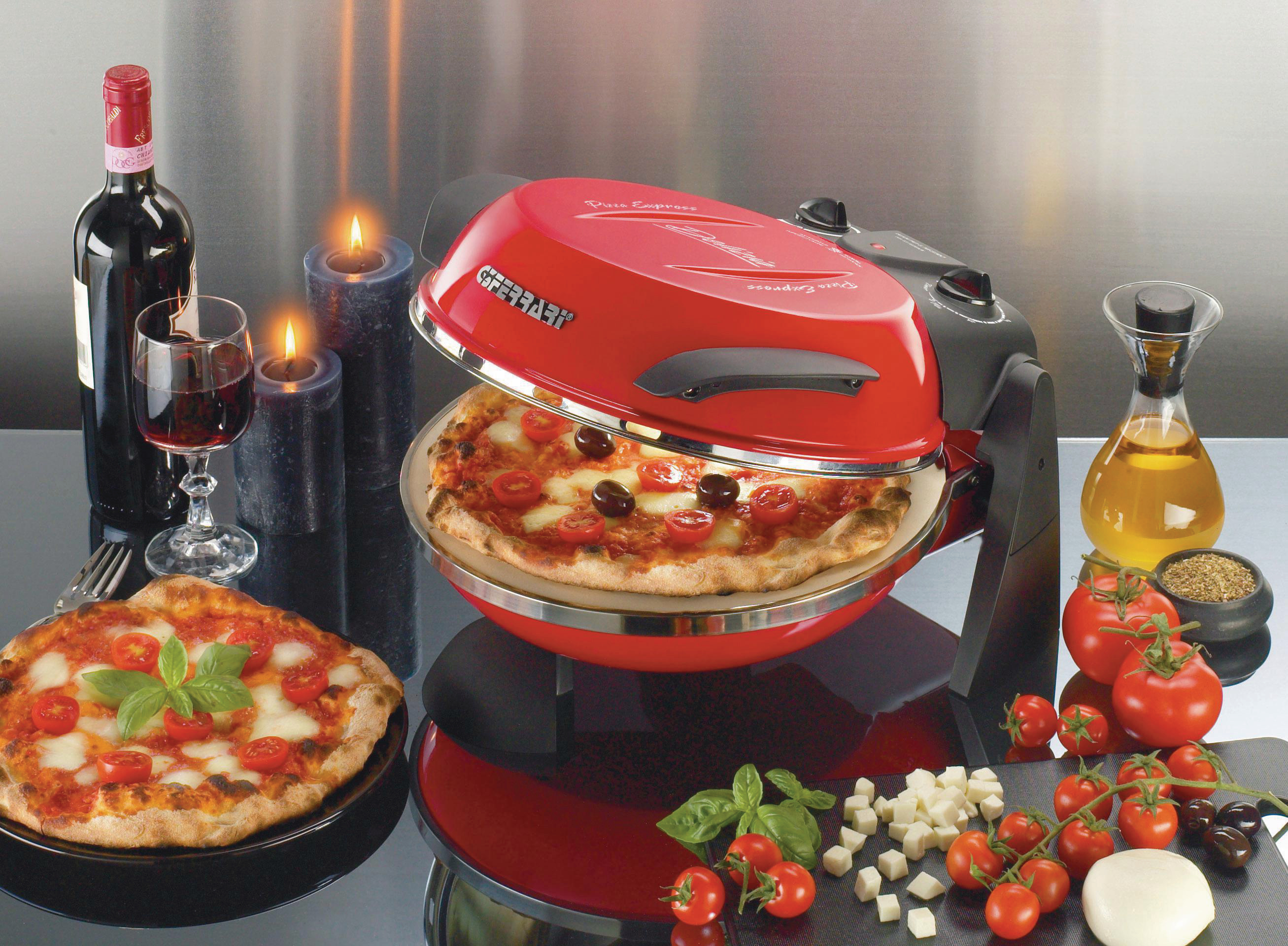 Ein roter Pizzaofen mit Pizza, Wein, Kerzen und Zutaten auf einem Tisch.