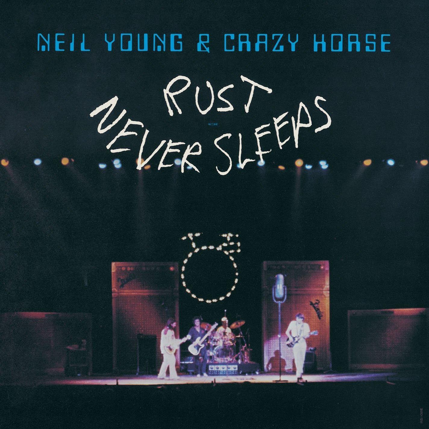 Neil Young & Crazy Horse album borítója. A cím: 'Rust Never Sleeps'. A zenekar a színpadon, hangszereket játszik a színpadi fények alatt. Sötét háttér.